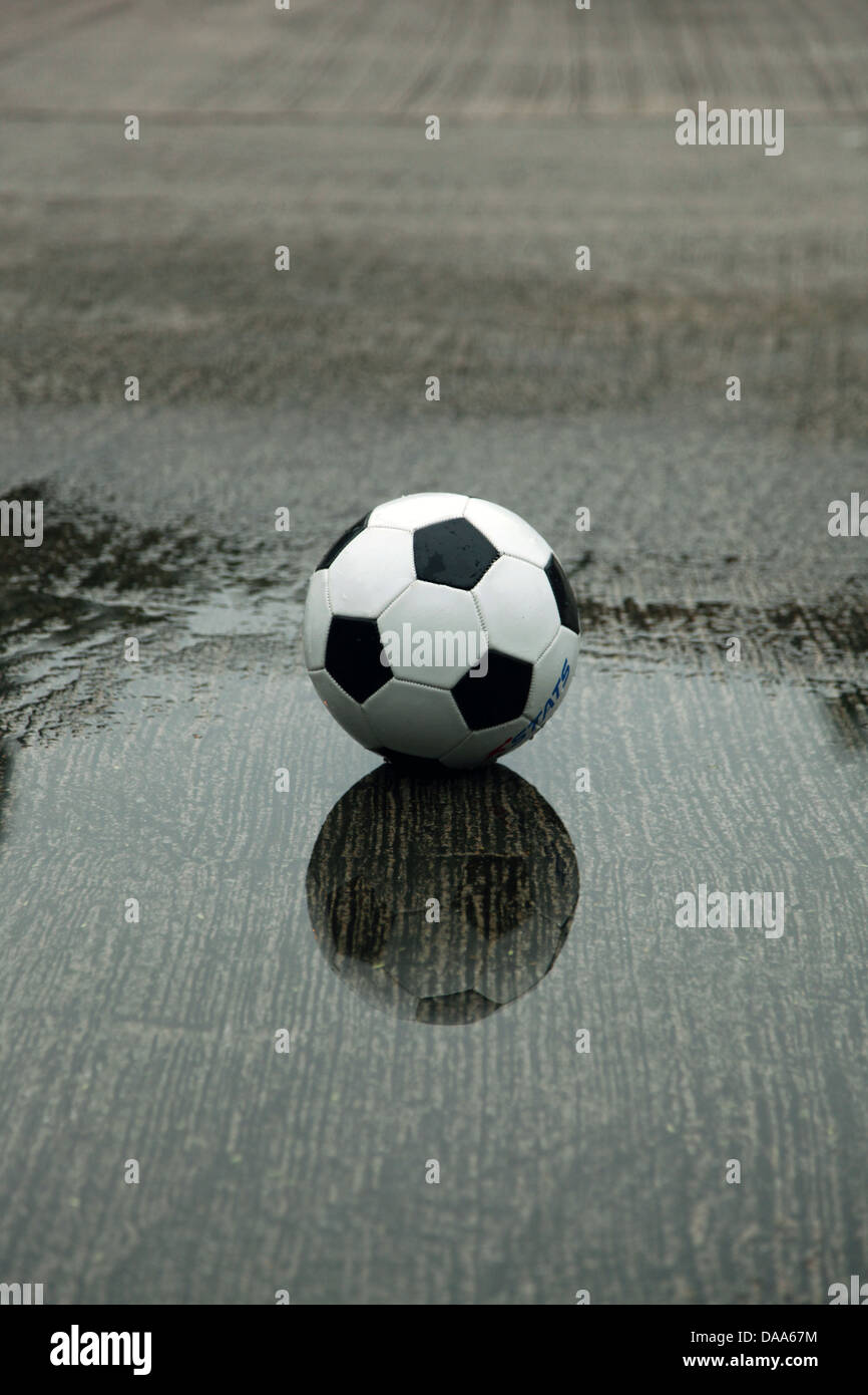 Es ist ein Foto von einem Fußball-Ball, der auf eine nasse Spielplatz in einer Wasserpfütze steht Stockfoto