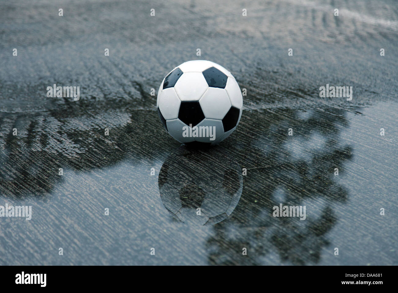 Es ist ein Foto von einem Fußball-Ball, der auf eine nasse Spielplatz in einer Wasserpfütze steht Stockfoto