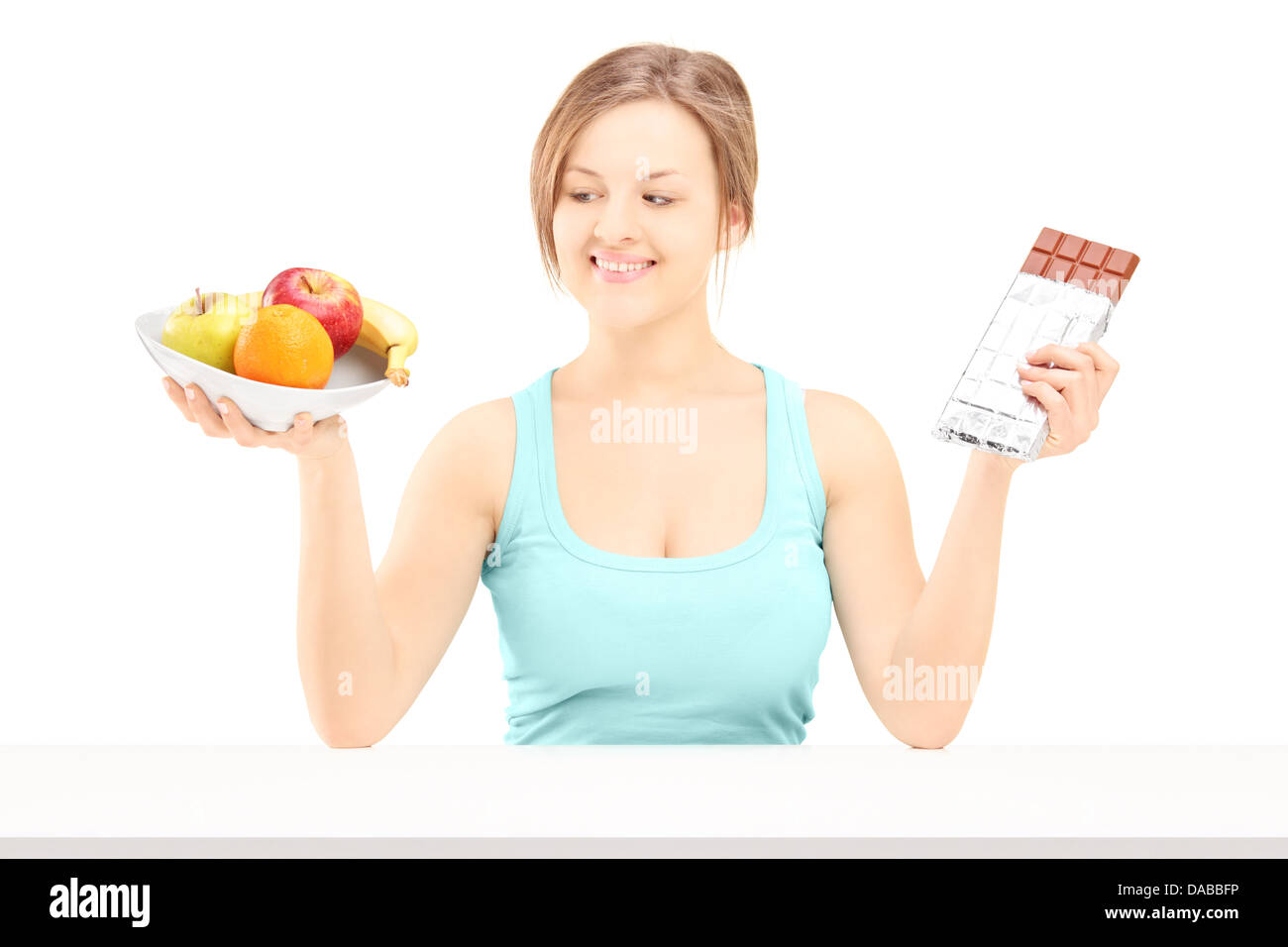 Junge Frau hält eine Schale mit frischem Obst und Schokolade, versuchen zu entscheiden, was man zu essen Stockfoto