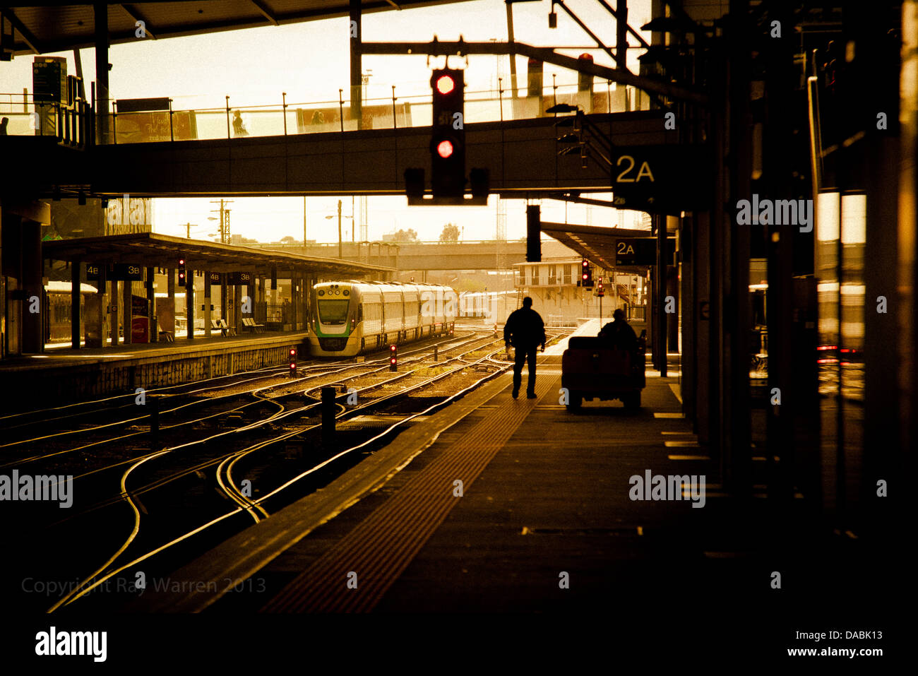 Eine Person ist im Gegenlicht Silhouette, wie er auf einer leeren Plattform in einem höhlenartigen Bahnhof auf einen Zug wartet. Stockfoto