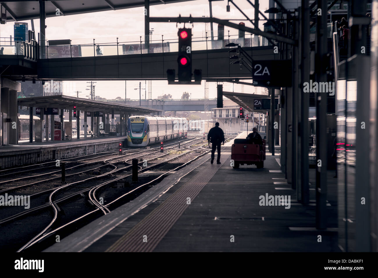 Eine Person ist im Gegenlicht Silhouette, wie er auf einer leeren Plattform in einem höhlenartigen Bahnhof auf einen Zug wartet. Stockfoto