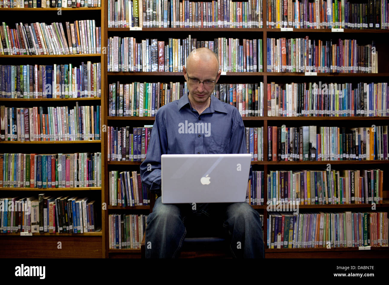 Cape Town-Südafrika-Michael sitzt auf Stuhl in Bibliothek arbeiten am Laptop, den er von Regalen Bücher 25. Februar 2013 umgeben ist. Stockfoto