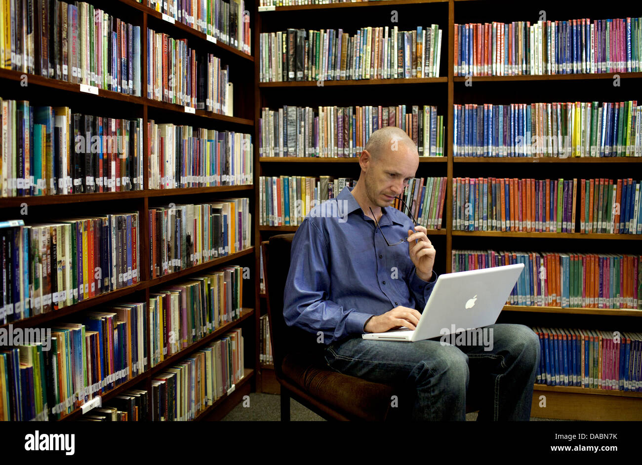 Cape Town-Südafrika-Michael sitzt auf Stuhl in Bibliothek arbeiten am Laptop, den er von Regalen Bücher 25. Februar 2013 umgeben ist. Stockfoto