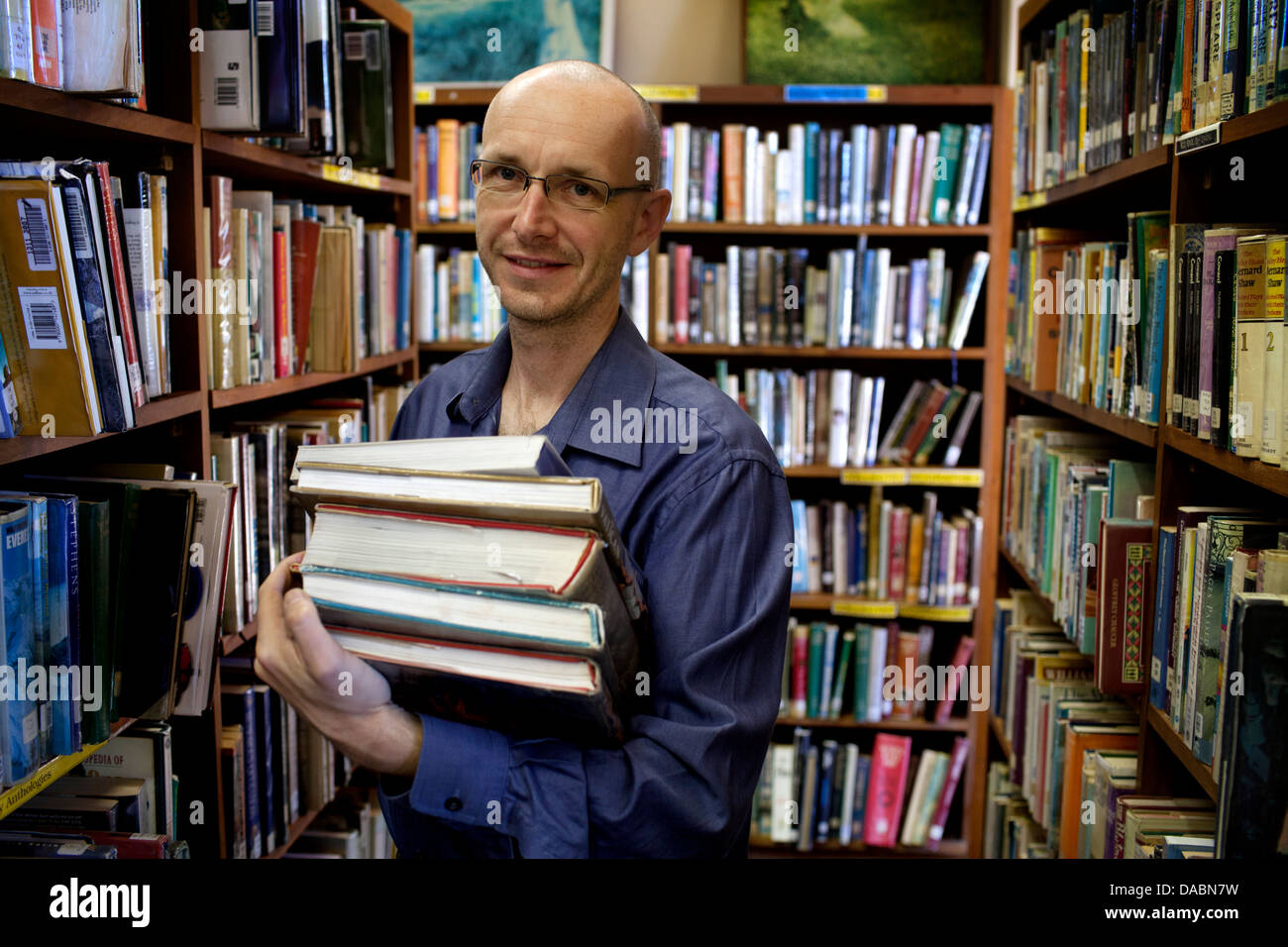 Cape Town, Südafrika. Michael hält Bücher in einer Bibliothek. Er ist umgeben von Regalen Bücher. 25. Februar 2013. Stockfoto