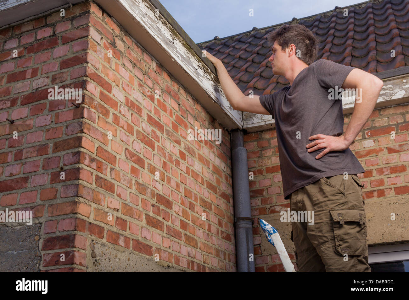 Junger Mann, das Dach eines alten Hauses stehen auf einer Leiter Inspektion Stockfoto