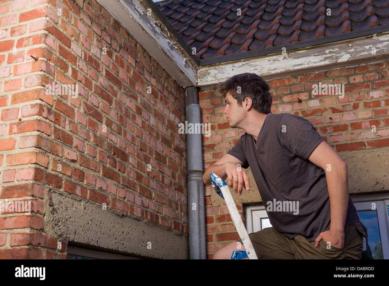 Junger Mann, die Inspektion der Wand eines alten Hauses stehen auf einer Leiter Stockfoto