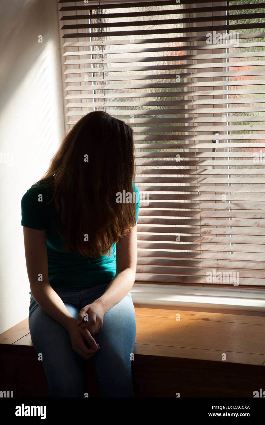 Ein junges Mädchen, Gesicht fallenden Haare, durch ein Fenster mit Licht herein. Stockfoto