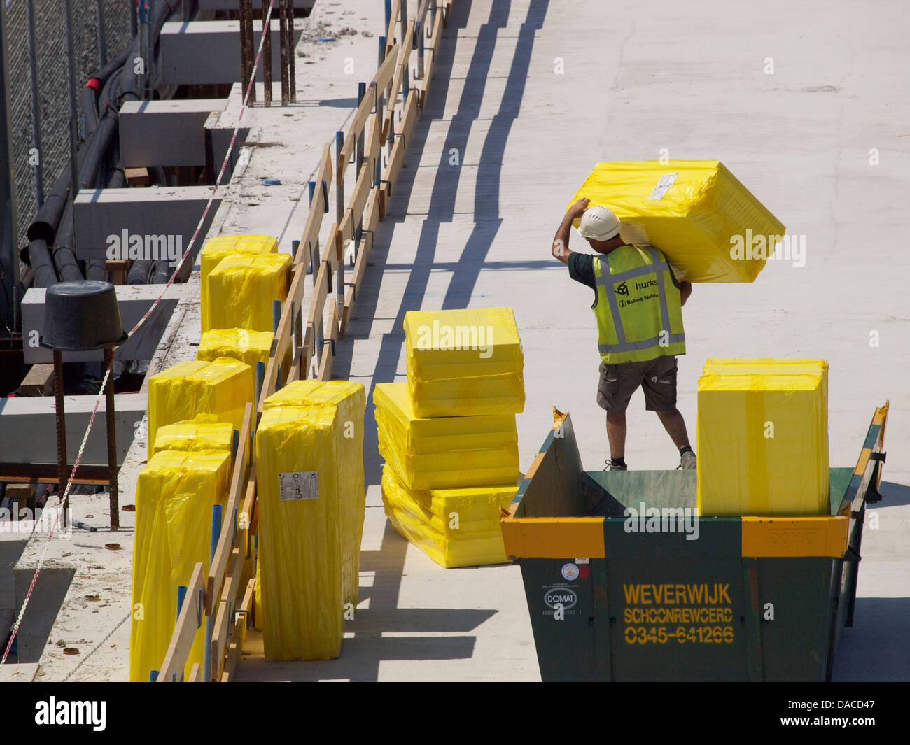 Mann auf Baustelle heben große gelbe Packung von Isolationsmaterial. Breda, Niederlande Stockfoto