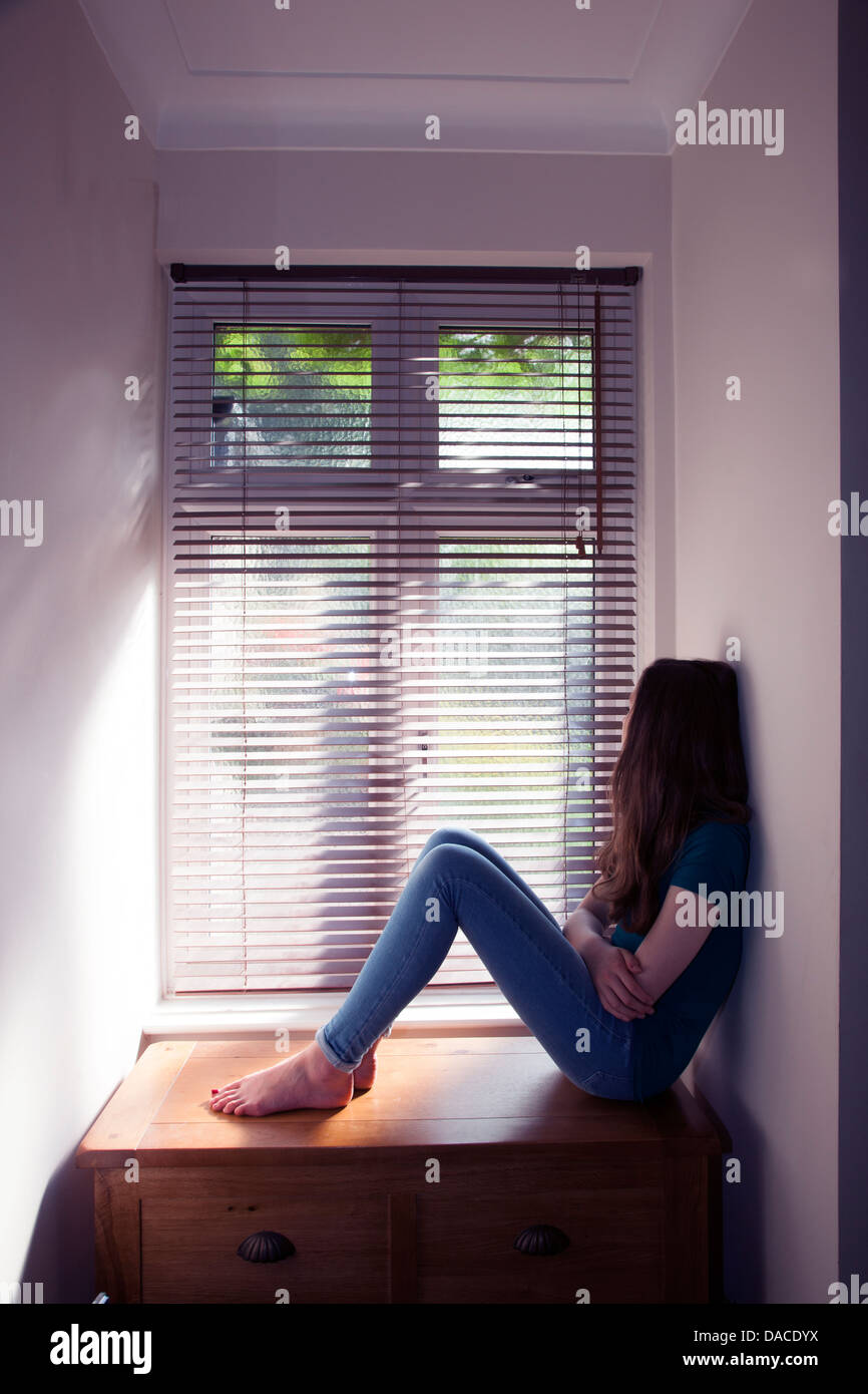 Ein junges Mädchen, sitzend an einem Fenster mit Licht herein. Hinten/Seitenansicht. Stockfoto