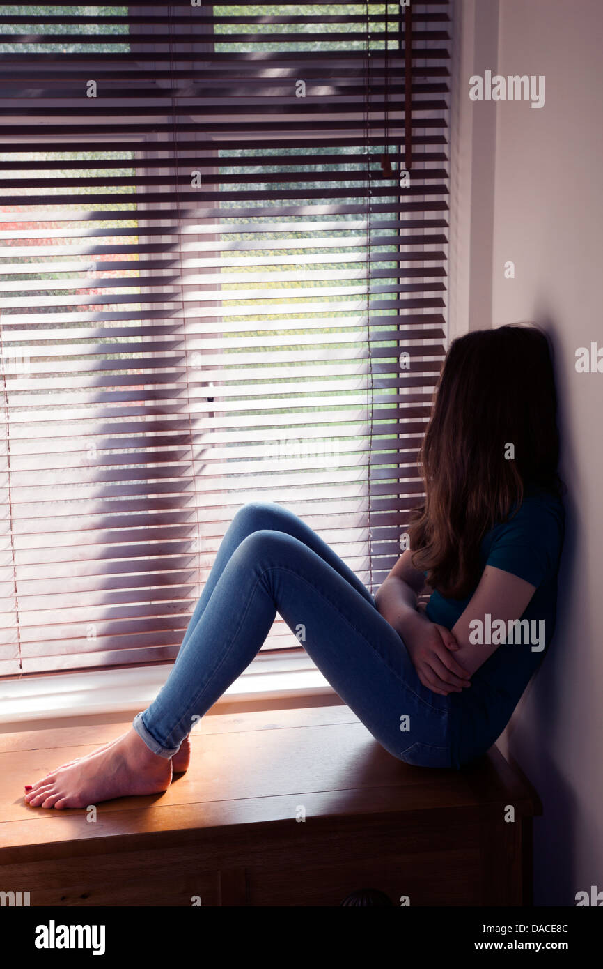 Ein junges Mädchen, sitzend an einem Fenster mit Licht herein. Hinten/Seitenansicht. Stockfoto