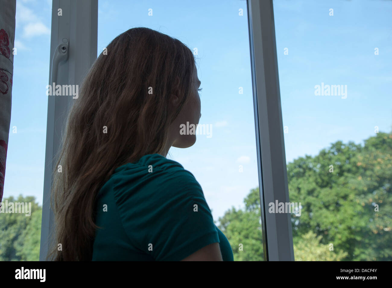 Ein junges Mädchen, Blick aus dem Fenster. Hinten/Seitenansicht. Stockfoto