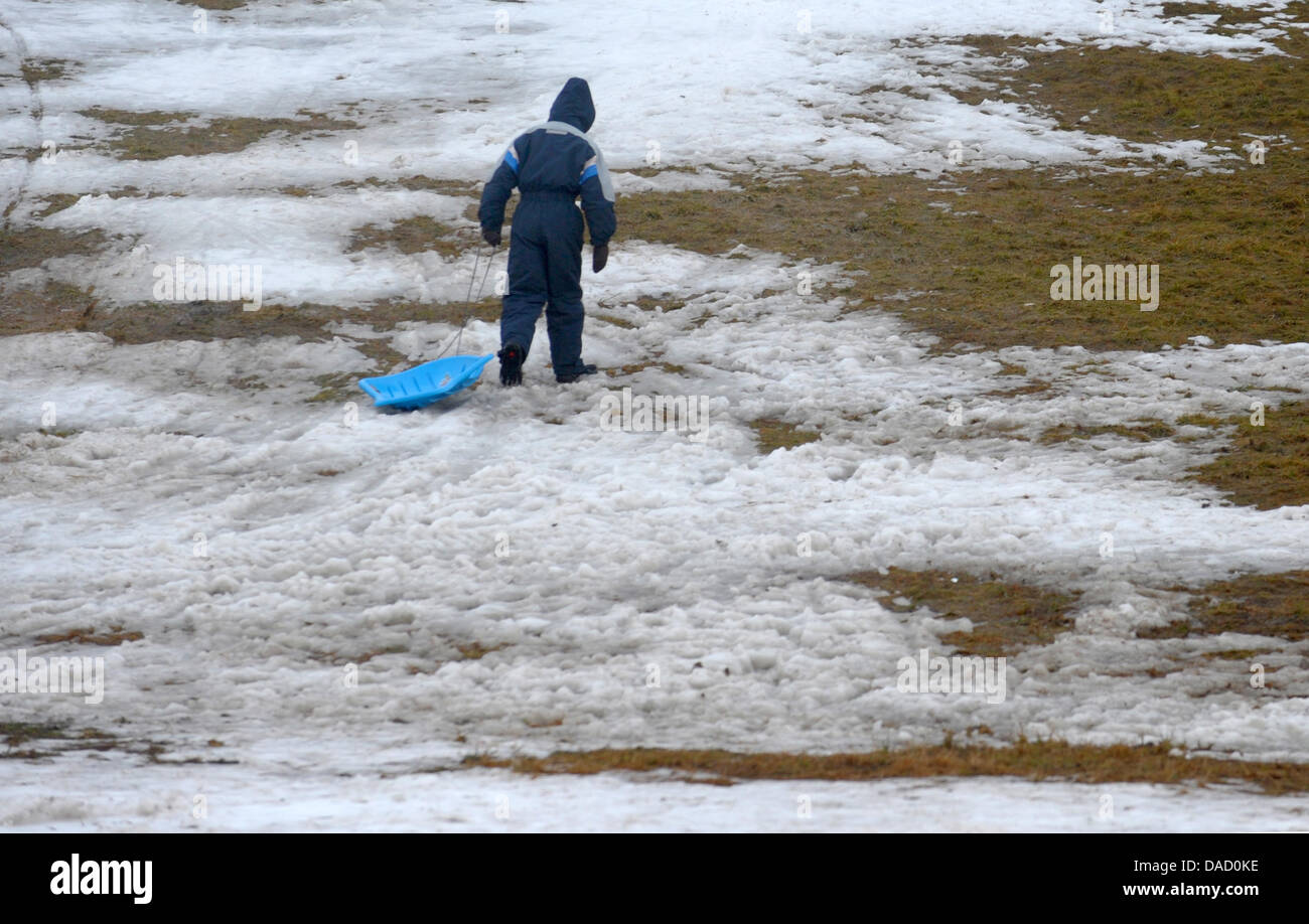 Ein Kind zieht seinen Schlitten eine Skipiste, die kaum von Schnee in Altenberg, Sachsen, 28. Dezember 2011 bedeckt ist. Die milden Temperaturen machen den Einsatz von Schneekanonen unmöglich. Foto: Matthias Hiekel Stockfoto