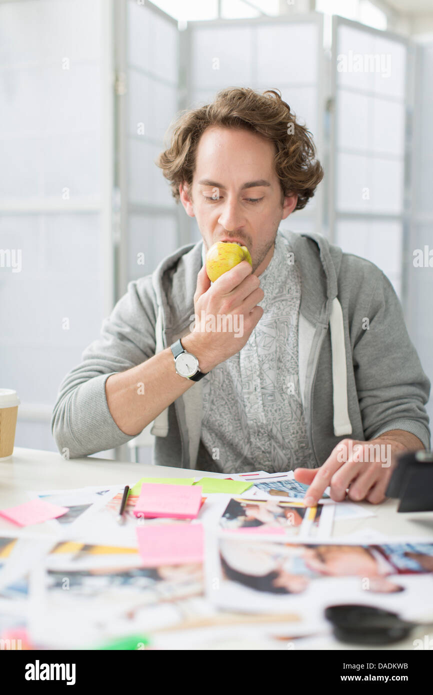 Junger Mann Essen Apfel am Schreibtisch im Kreativbüro Stockfoto