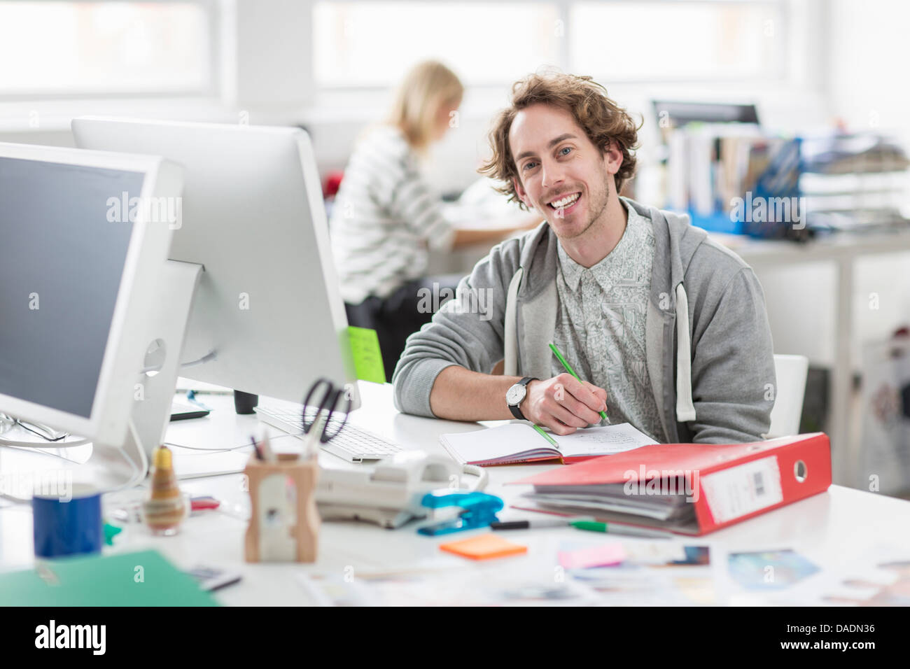 Junger Mann am Schreibtisch sitzen und lächelnd in Kreativbüro, Porträt Stockfoto