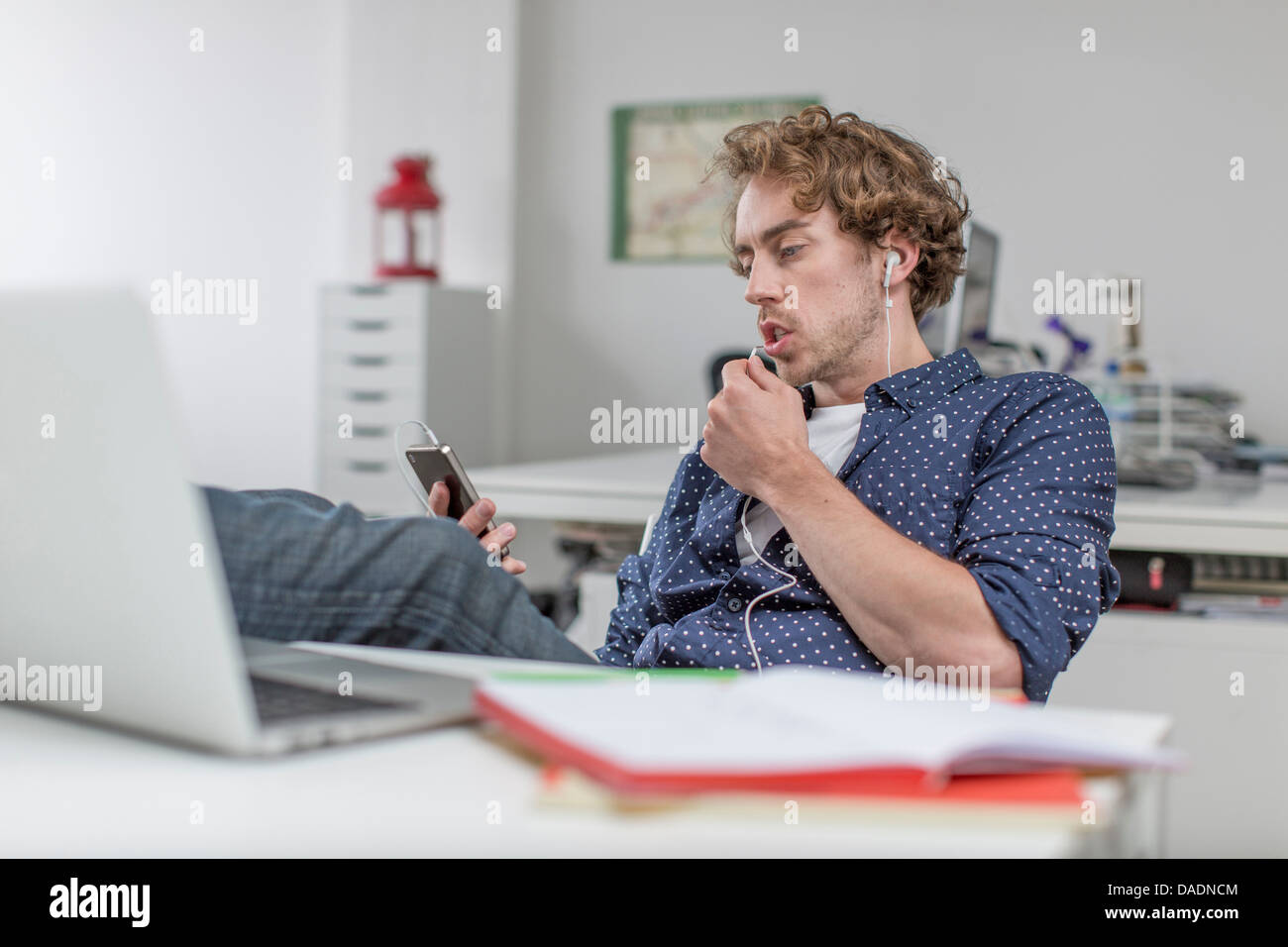 Junge Büroangestellte anhören von MP3-Player am Schreibtisch Stockfoto
