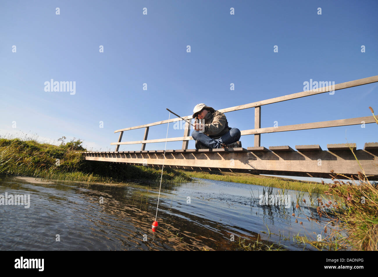 Junge sitzt im Schneider Sitz auf einer Holzbrücke und Angeln, Niederlande, Norden der Niederlande Stockfoto