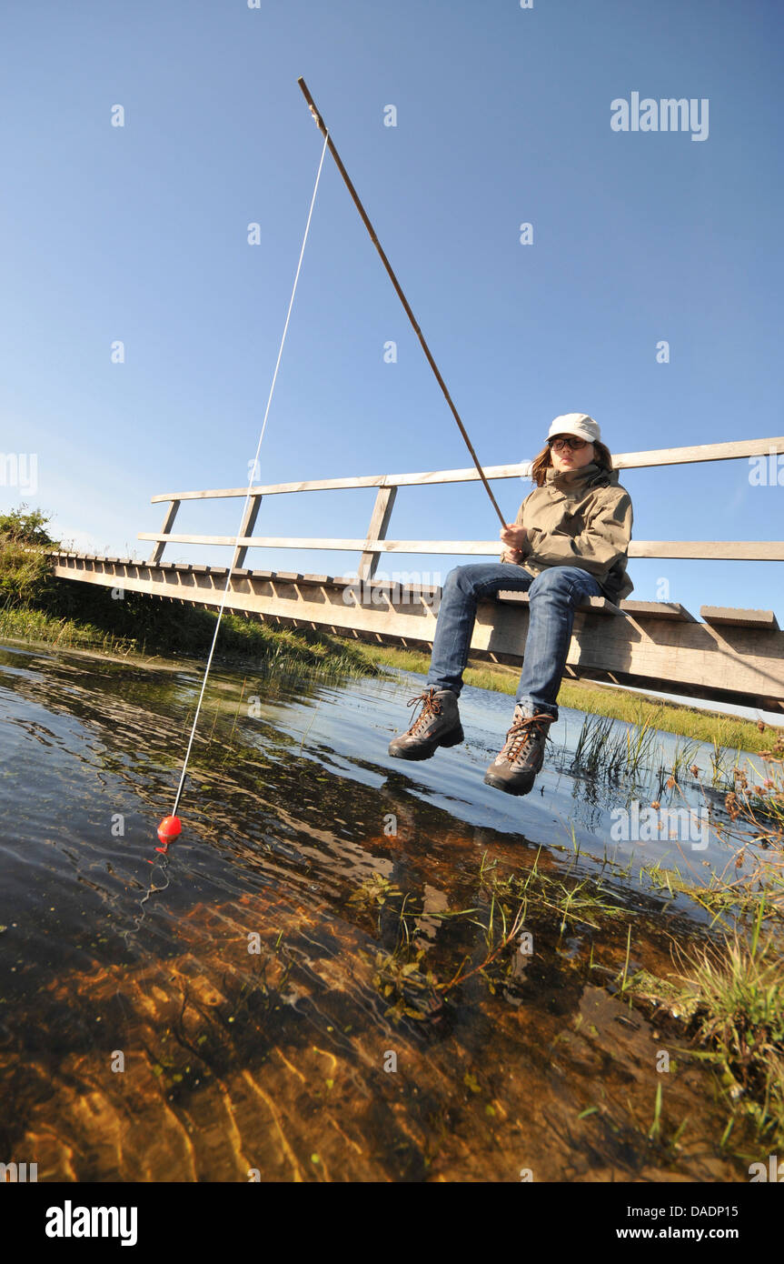 Junge sitzt auf einer hölzernen Brücke und Angeln, Niederlande, Norden der Niederlande Stockfoto