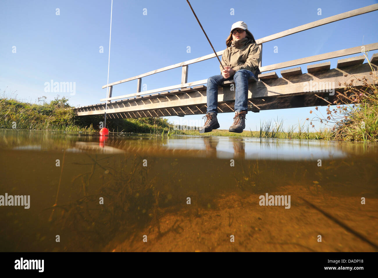 Junge sitzt auf einer hölzernen Brücke und Angeln, Niederlande, Norden der Niederlande Stockfoto