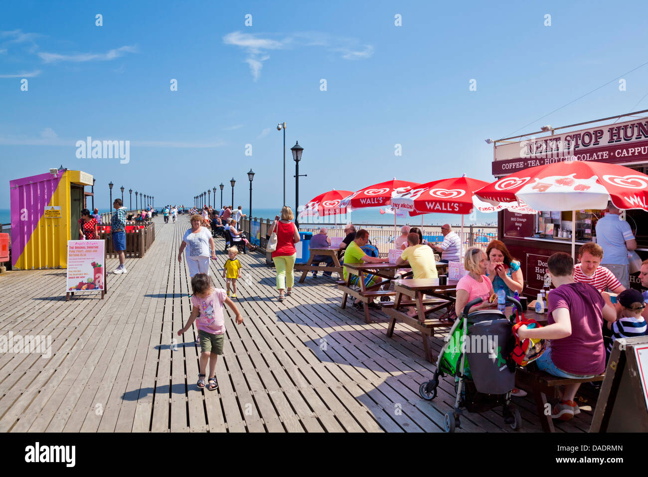 Touristen vor einem Café mit Sonnenschirmen auf dem Pier in Skegness an einem sonnigen Tag Lincolnshire England UK GB EU Europa Stockfoto