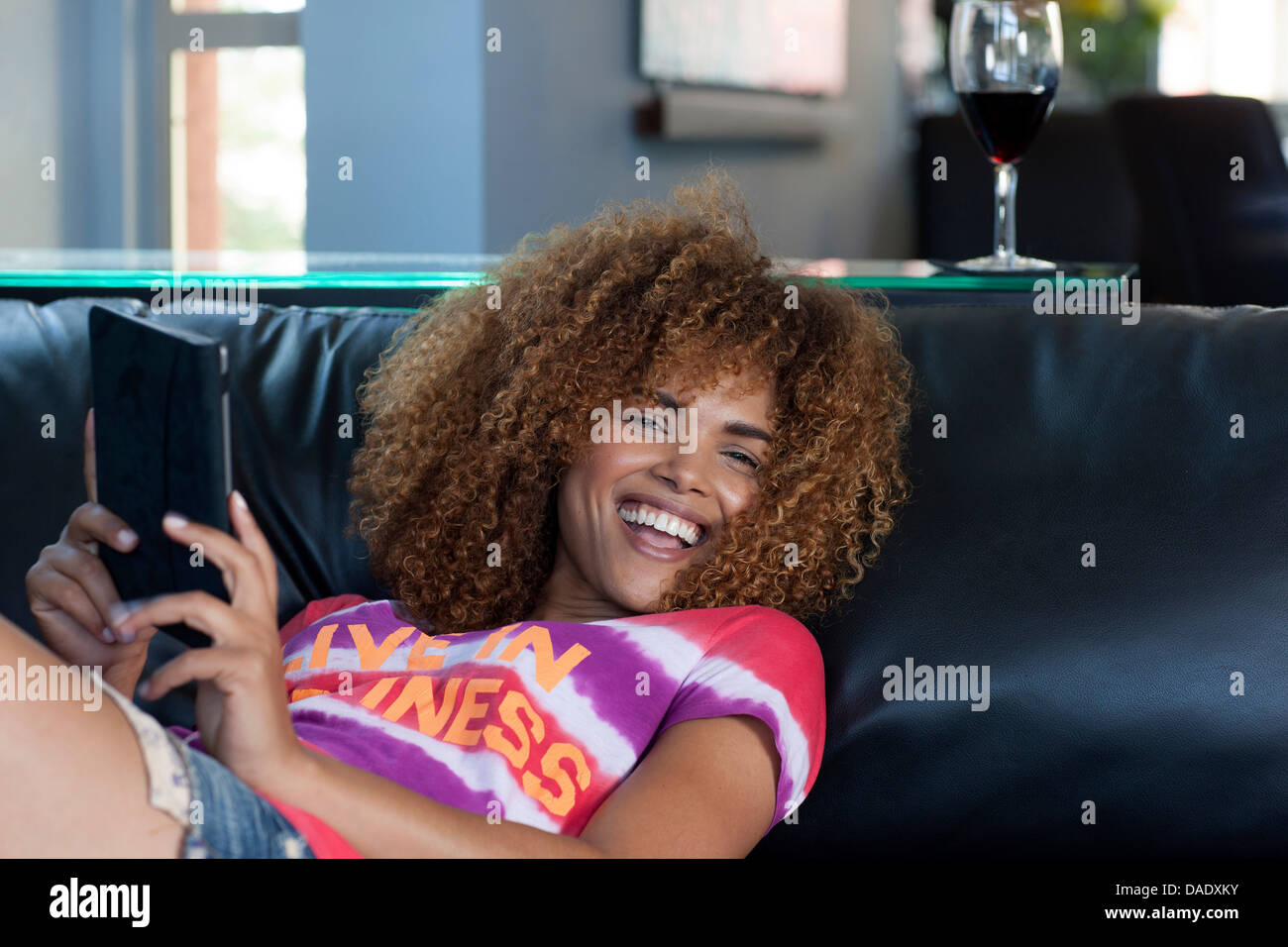 Mitte Erwachsene Frau sitzen Holding elektronisches Buch auf Sofa Lächeln Stockfoto