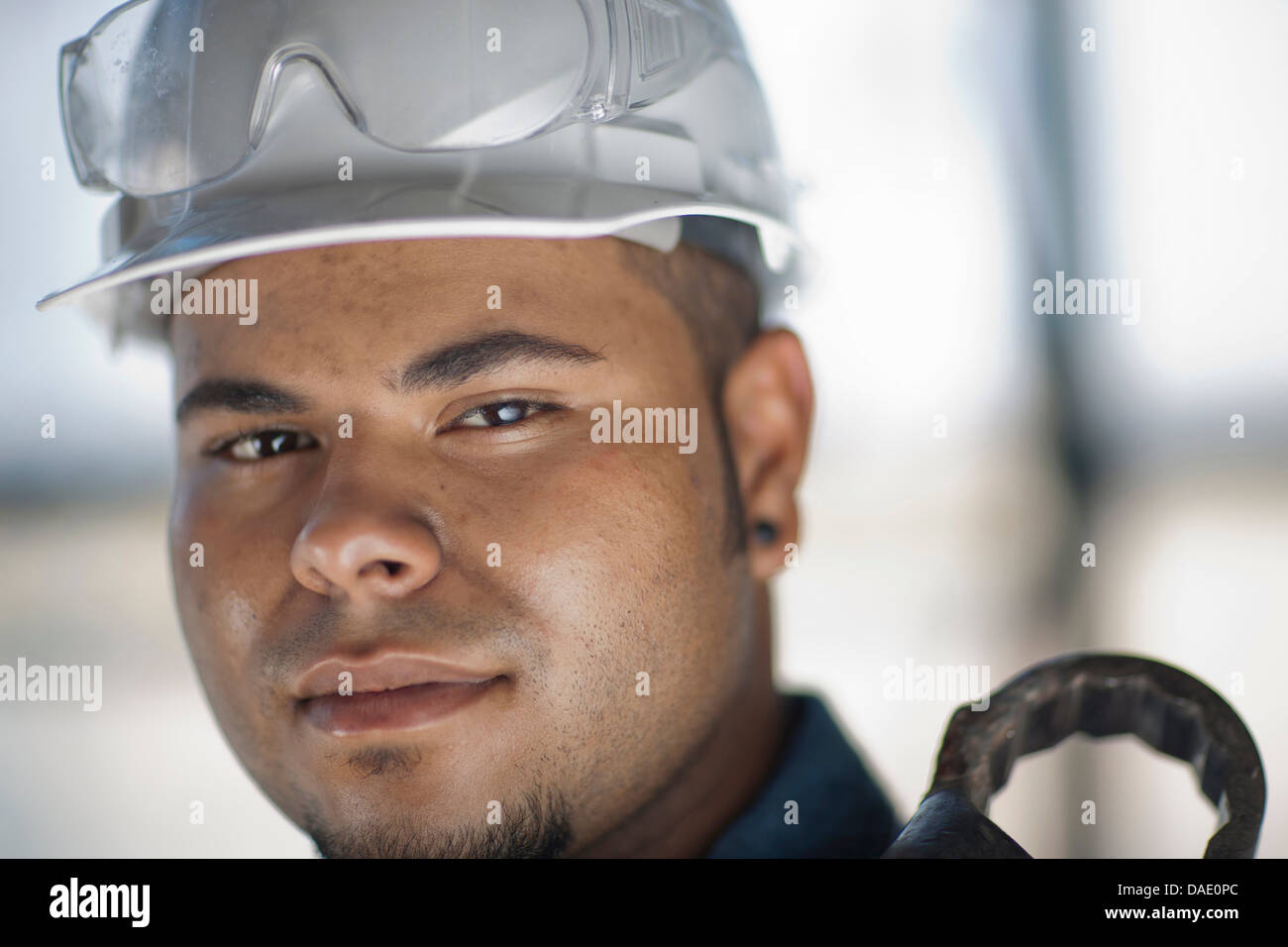 Junge Bauarbeiter tragen Schutzhelm und Holding Schraubenschlüssel, Lächeln Stockfoto