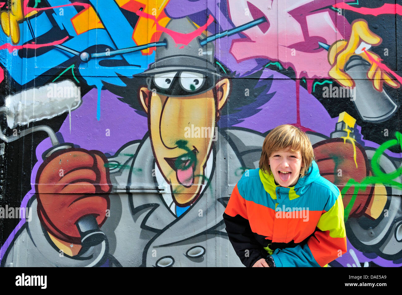 zwölf Jahre alten Jungen stehen vor einer Graffitiwand und pocking die Zunge heraus, Deutschland, Nordrhein-Westfalen, Köln Stockfoto