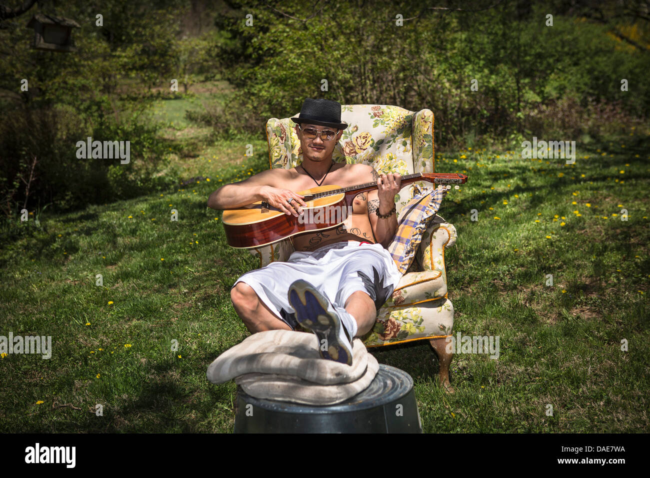 Mann spielt Gitarre in Sessel in Garten Stockfoto