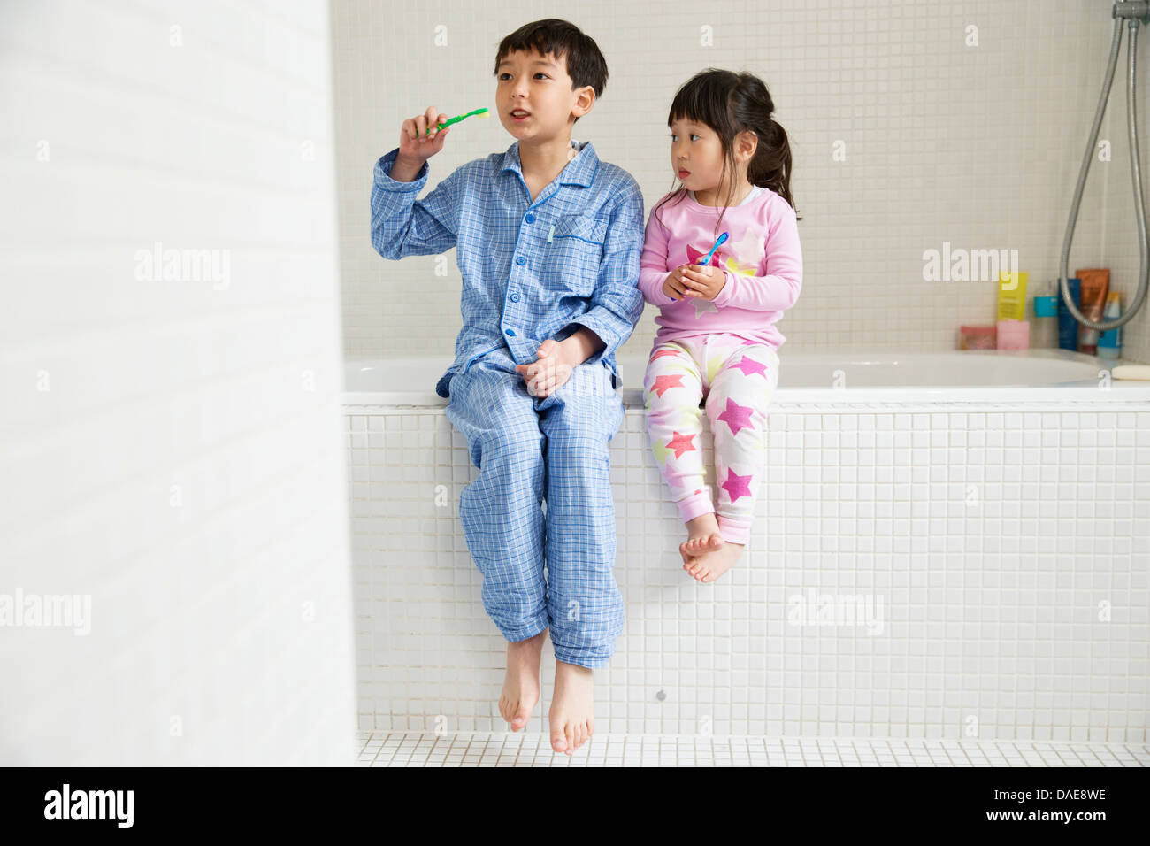 Bruder und Schwester sitzen am Rand der Badewanne mit Zahnbürsten Stockfoto