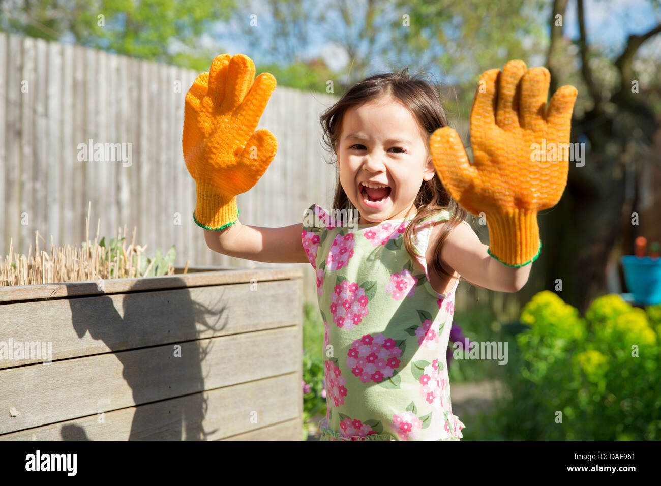 Junges Mädchen im Garten mit übergroßen Handschuhen Stockfoto