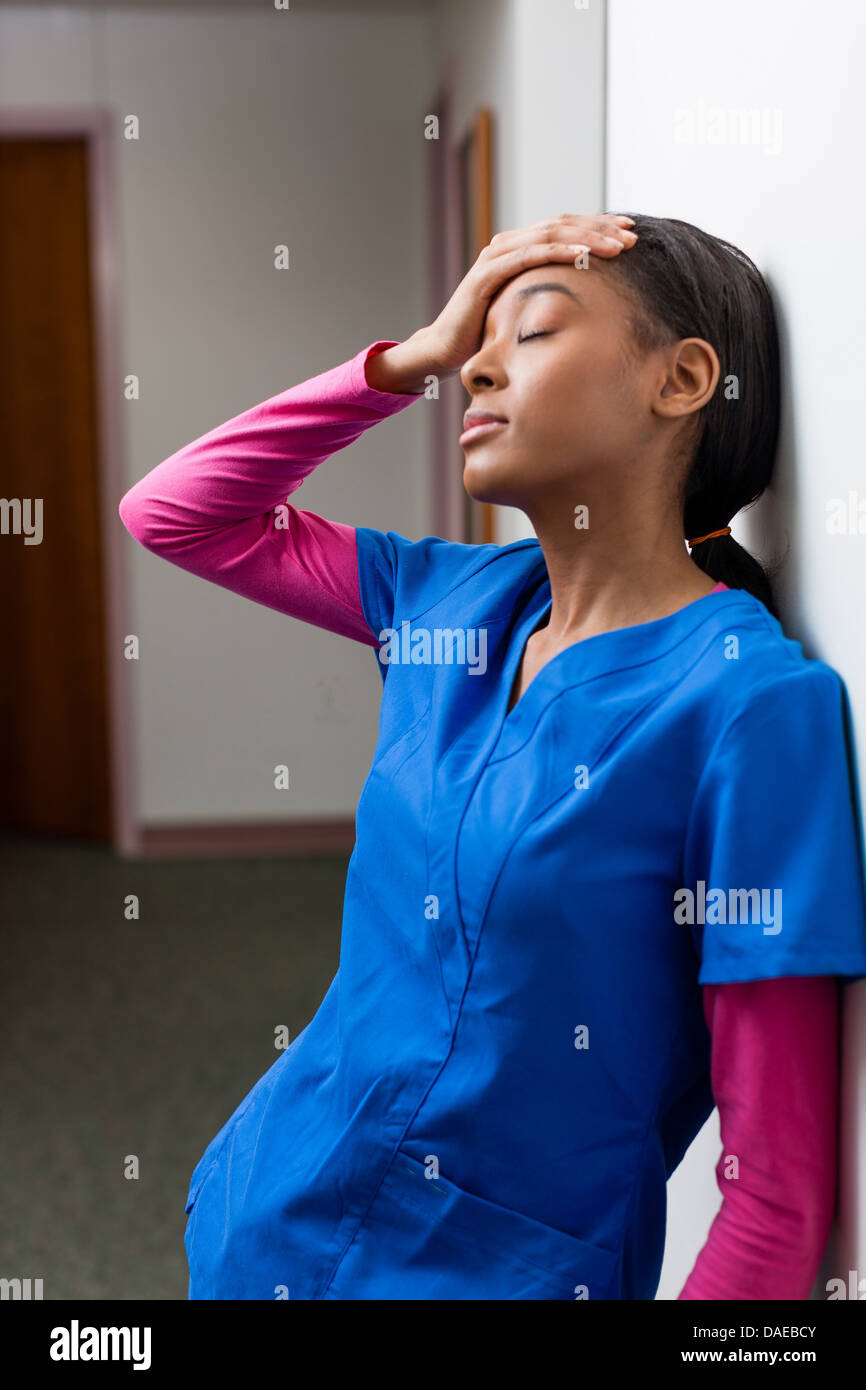 Krankenschwester mit geschlossenen Augen und hand auf Kopf im Krankenhausflur Stockfoto