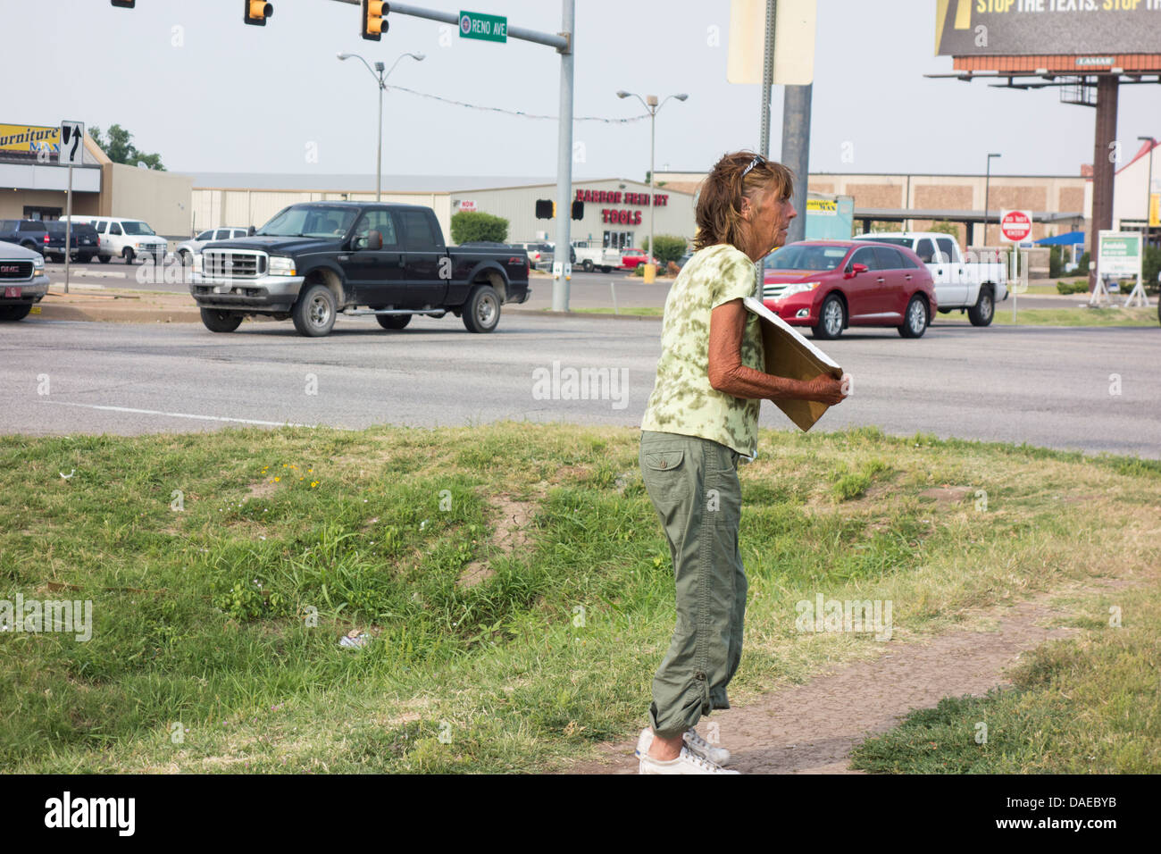 Eine alte, obdachlose Frau mit einem Schild bittet an einer Kreuzung in Oklahoma City, Oklahoma, USA in einem hohen Verkehr Bereich. Stockfoto