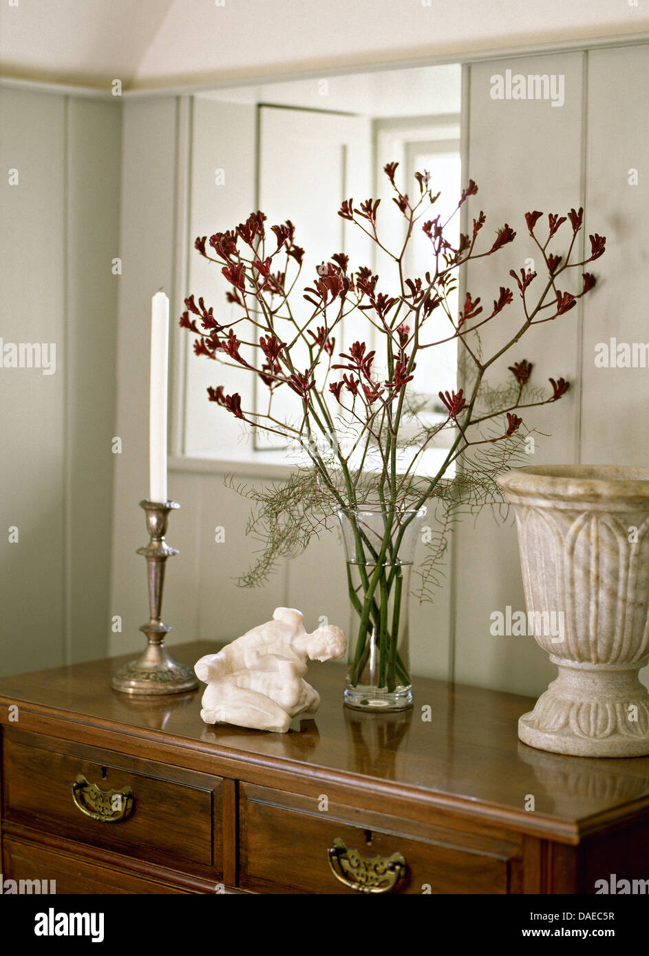 Graue Hütte Halle mit Blüten in der Knospe in Glasvase auf antike Kommode mit Stein Urn und Silber Kerzenhalter Stockfoto