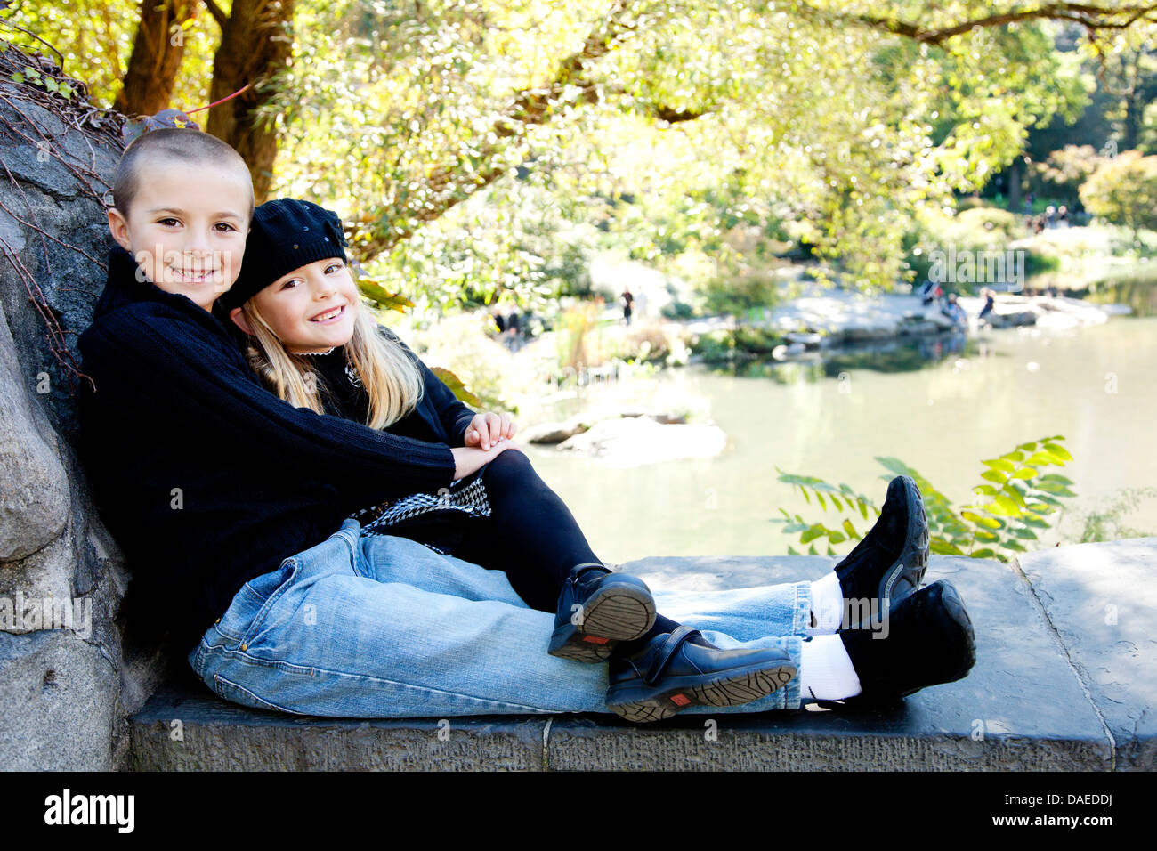 Lächelnden jungen und Mädchen sitzen auf steinernen Sims im Park, Porträt Stockfoto