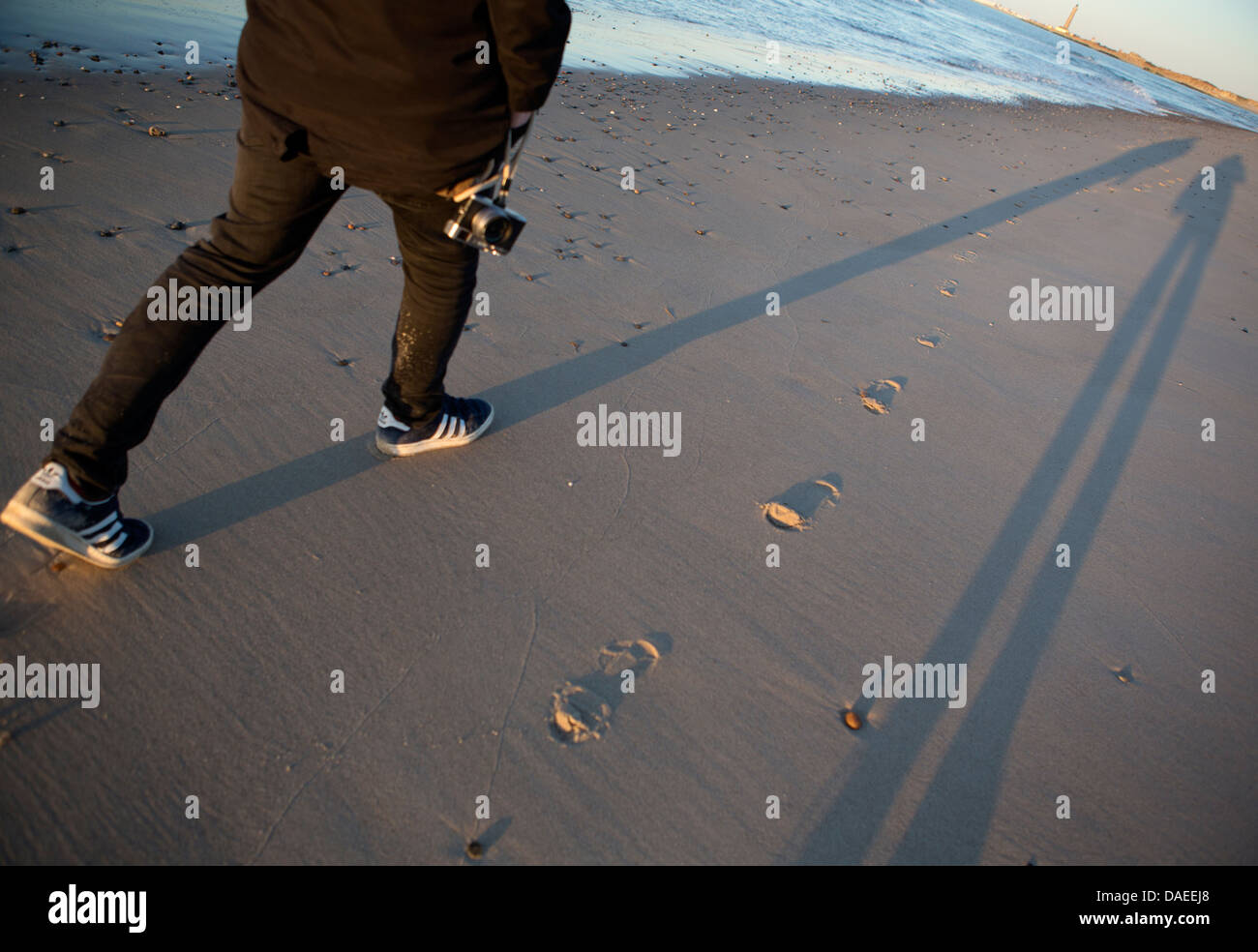 Beine eines Mannes in schwarz zu Fuß am Strand mit seiner Kamera gekleidet Stockfoto