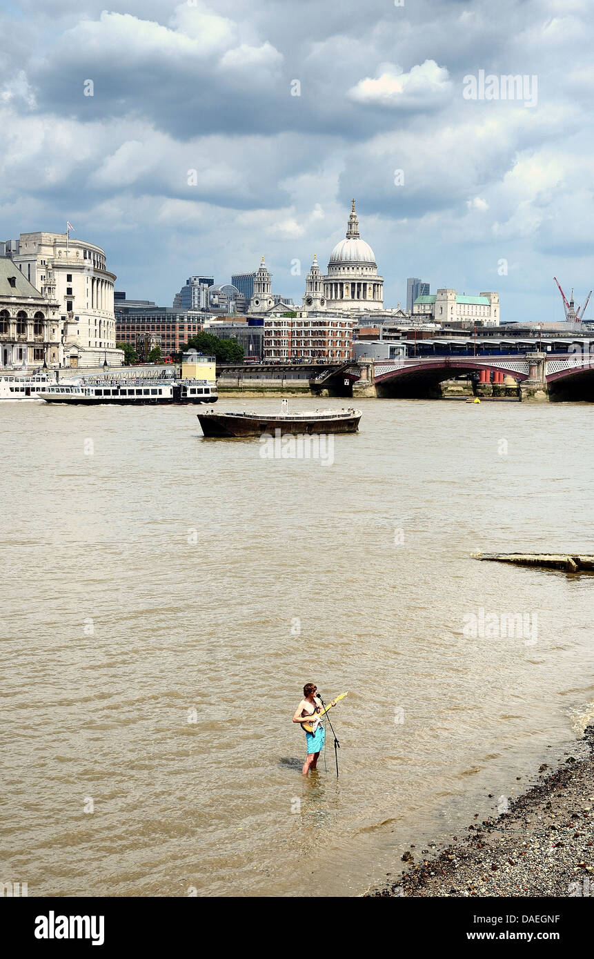 Straßenmusikant in der Themse mit City of London im Hintergrund stehen Stockfoto