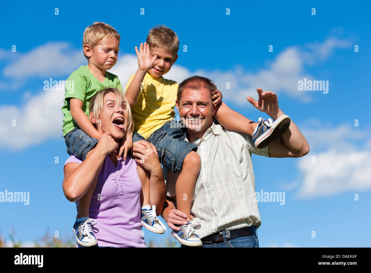 Familie mit zwei kleinen Jungen auf einer Sommerwiese - tragen die Eltern die Söhne auf ihren Schultern Stockfoto