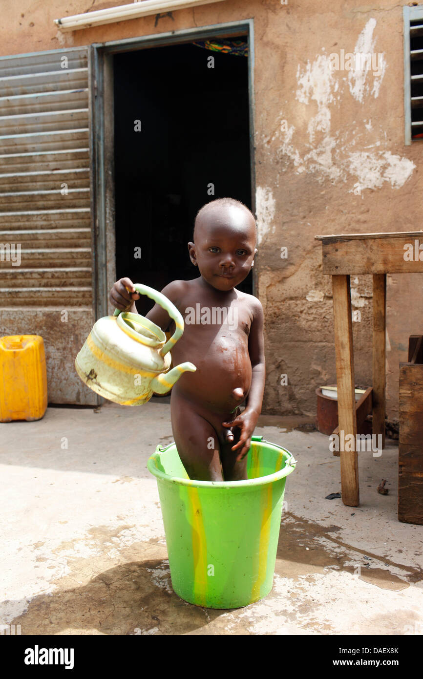 Ein kleiner Junge sitzt in einem Eimer und wäscht sich mit einem Topf gießen in der Burkinan Hauptstadt Ouagadougou, Burkina Faso, 14. Oktober 2011. Foto: Florian Schuh Stockfoto