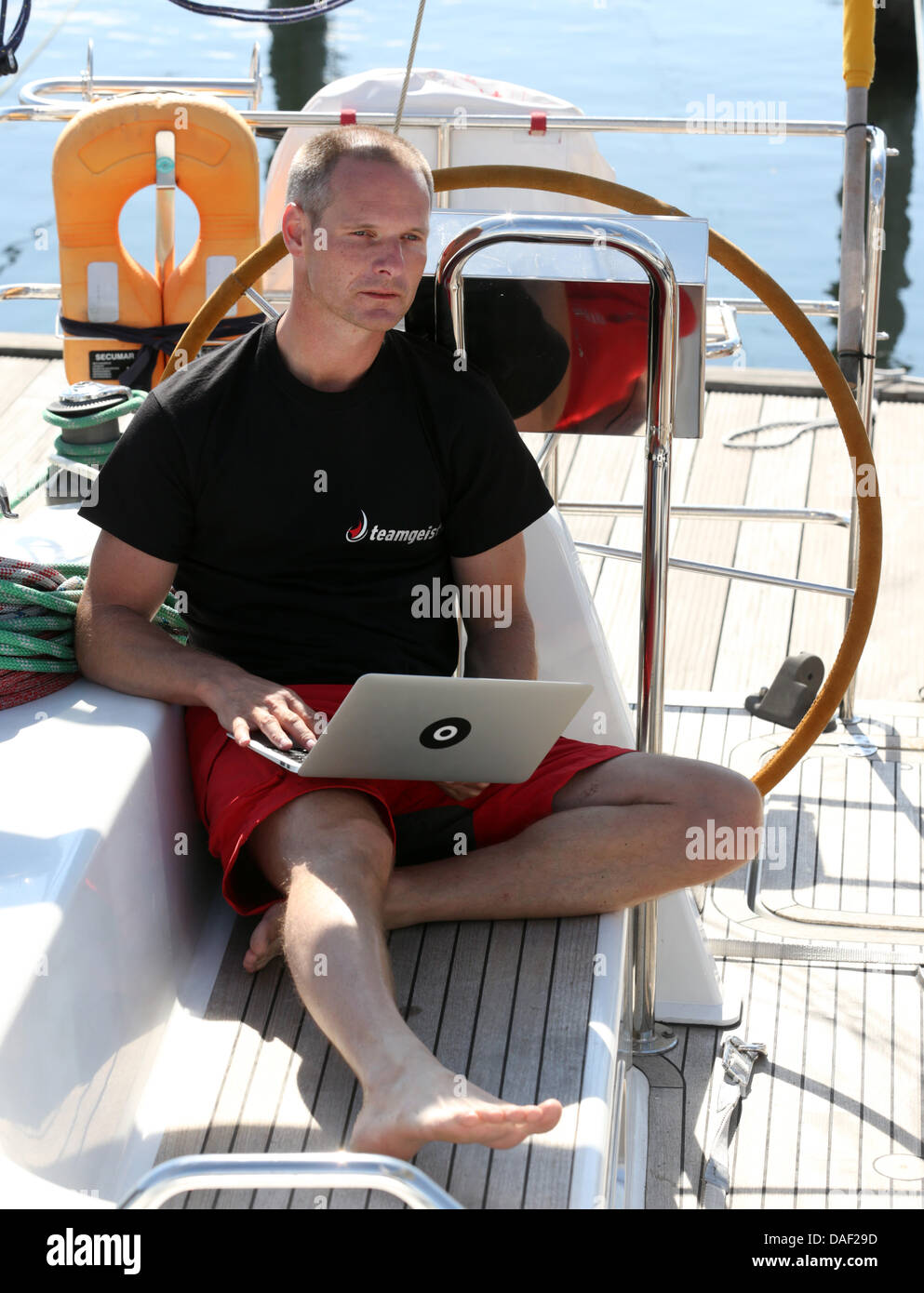 Michael Haufe, general Manager der Teamgeist GmbH in Heidsee, sitzt mit seinem Computer an Bord eines Segelbootes am Yachthafen Hohe Duene in Warnemünde, Deutschland, 6. Juli 2013. Haufe startet eine zweijährige Weltumrundung von dort, während der er seine Service-Unternehmen aus an Bord das Segelschiff gelingen wird. Foto: BERND WUESTNECK Stockfoto