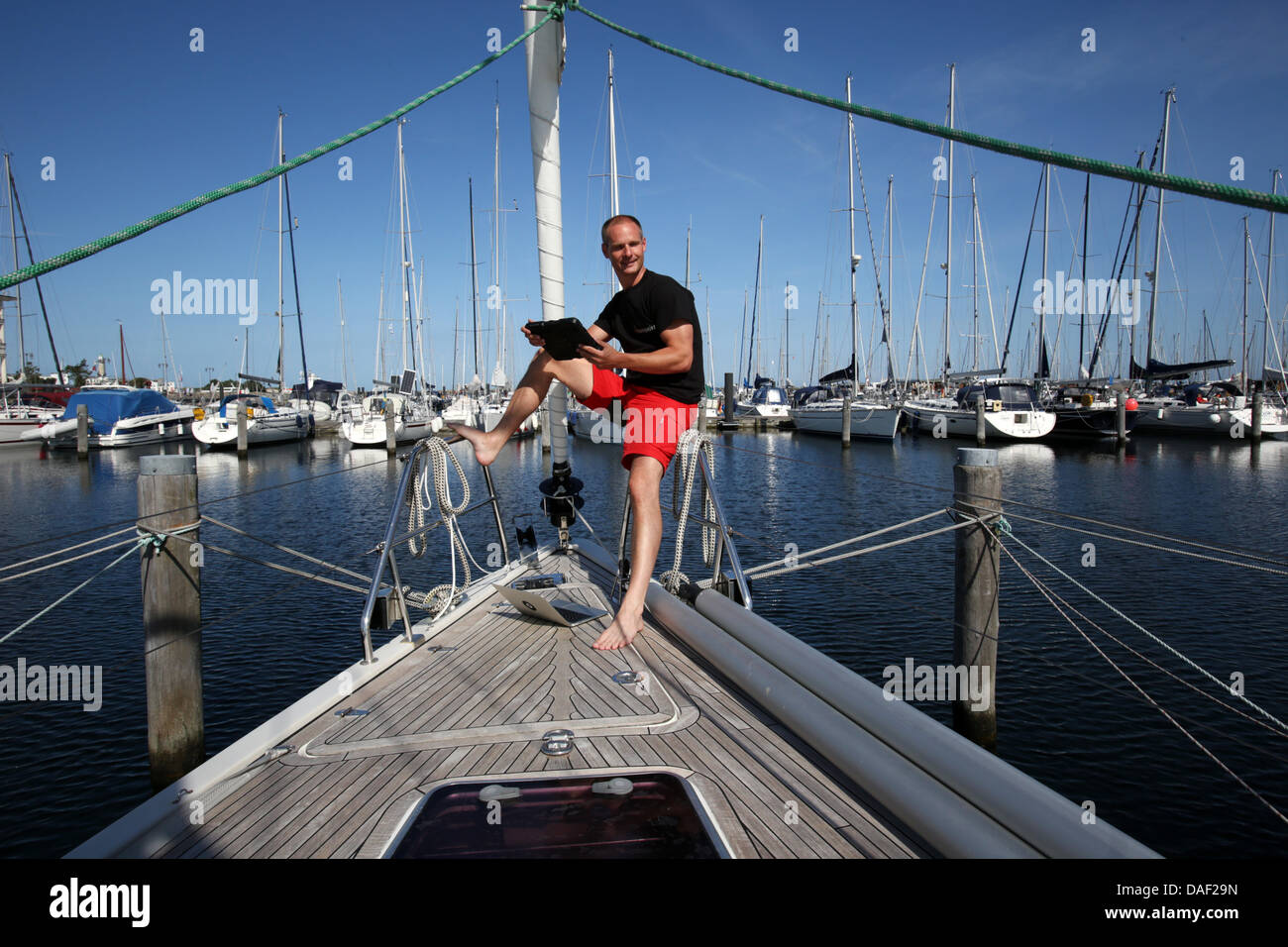 Michael Haufe, general Manager der Teamgeist GmbH in Heidsee, sitzt mit seinem Computer an Bord eines Segelbootes am Yachthafen Hohe Duene in Warnemünde, Deutschland, 6. Juli 2013. Haufe startet eine zweijährige Weltumrundung von dort, während der er seine Service-Unternehmen aus an Bord das Segelschiff gelingen wird. Foto: BERND WUESTNECK Stockfoto