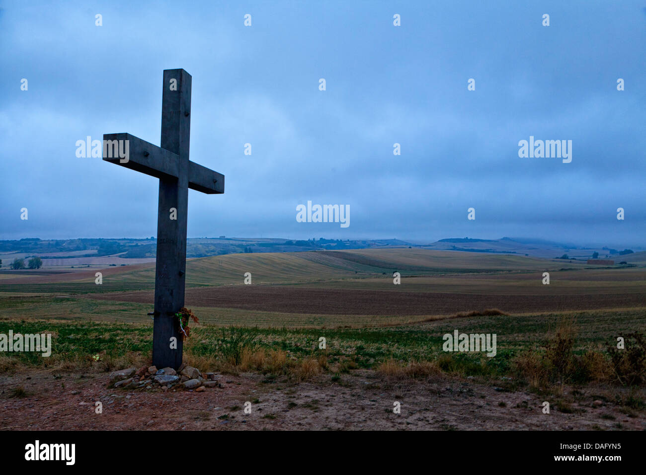 großes Kreuz neben der Camino-Straße. sanfte grüne Hügel und dunkle Wolken im Hintergrund. Cruz Los Vallentes, Granon Spanien. Stockfoto