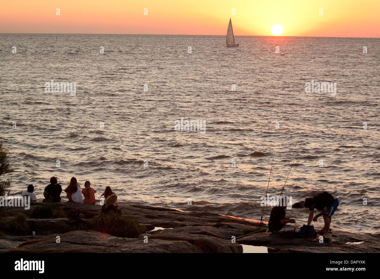 Menschen, die den Sonnenuntergang über den Rio De La Plata vom Ufer in Colonia del Sacramento, Uruguay Stockfoto