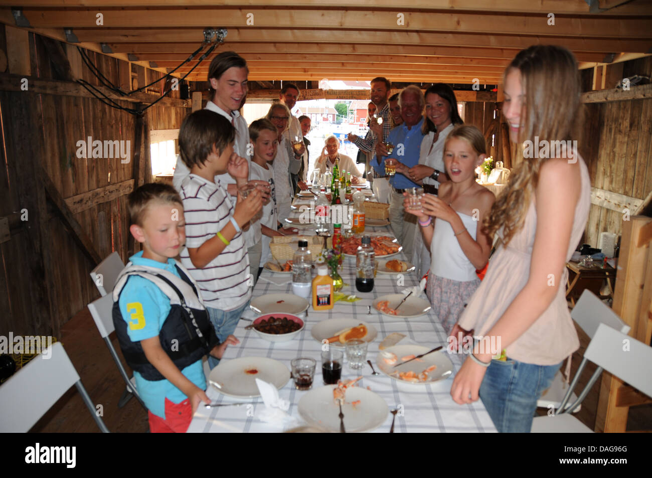 Großvaters Geburtstagsparty mit drei Familiengenerationen lächelnd am Tisch mit Kuchen, Kerzen und Kaffee im Bootshaus in Schweden Stockfoto