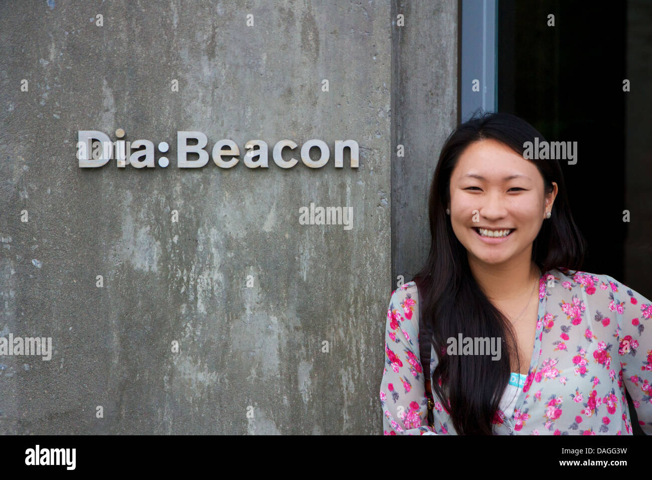 Asiatische Mädchen lächelt neben einem Schild kündigt Dia: Beacon-zeitgenössische Kunst-Institut im Hudson Valley in Beacon, New York, USA. Stockfoto