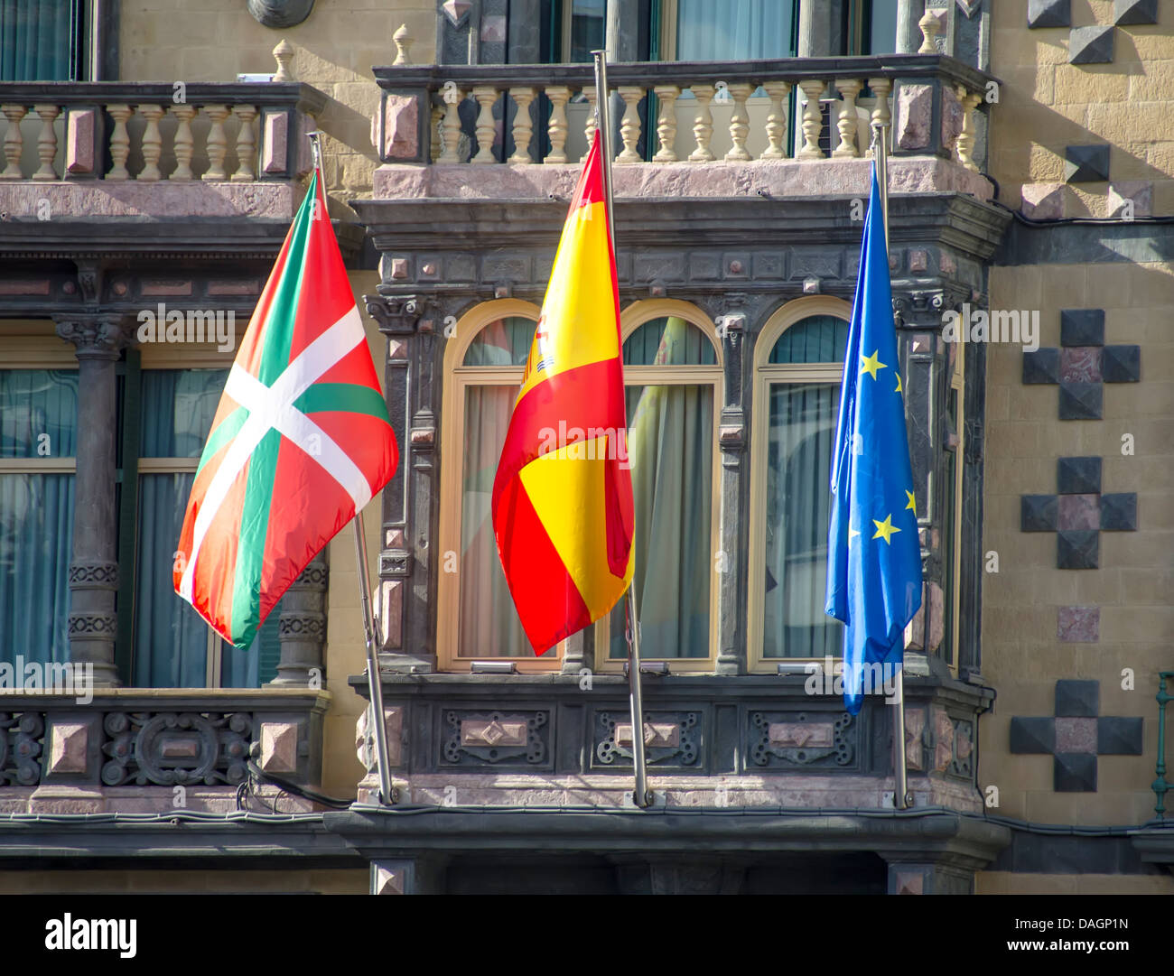 Fahnen der Baskenland, Spanien und der Europäischen Union winken in die Fassade eines Gebäudes Stockfoto