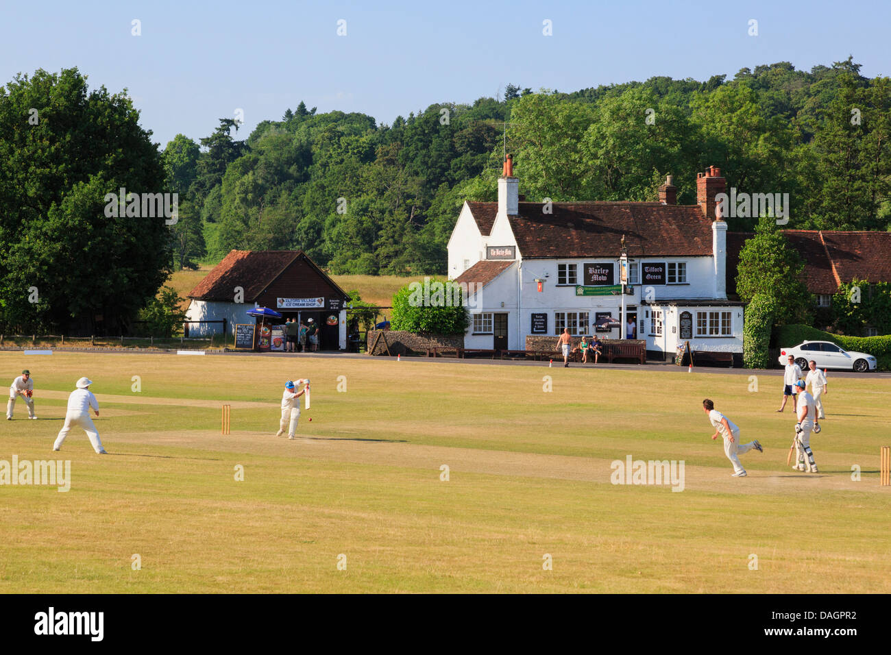 Lokale Teams spielen Cricket Match auf Village Green mit verbrannte Gras vor der Gerste Mähen Pub an einem Sommerabend. Tilford Surrey England Großbritannien Stockfoto