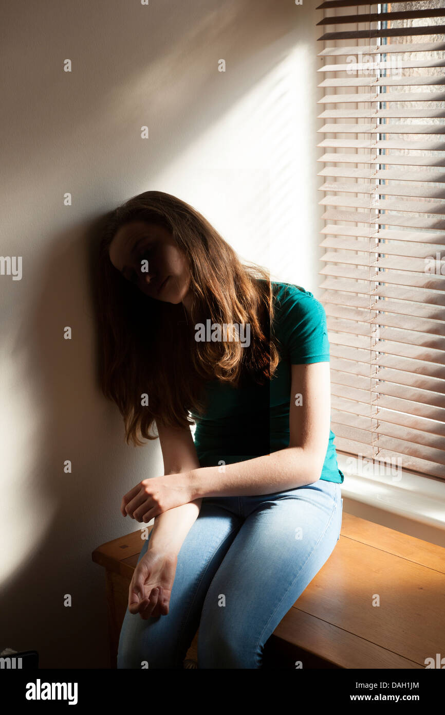Ein junges Mädchen, sackte sitzen gegen die Wand durch ein Fenster mit Licht herein. Stockfoto
