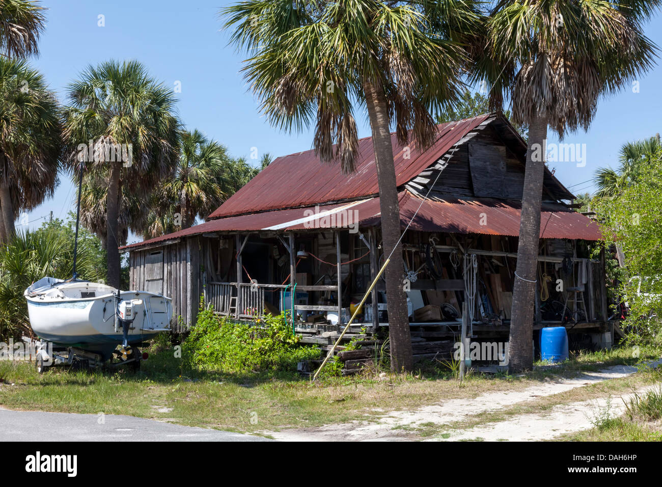 Eine alte heruntergekommene Holz Holzhaus mit Rosten Metalldach. Ein Segelboot auf einen Anhänger und Junk-Krempel Veranda und Garten. Stockfoto