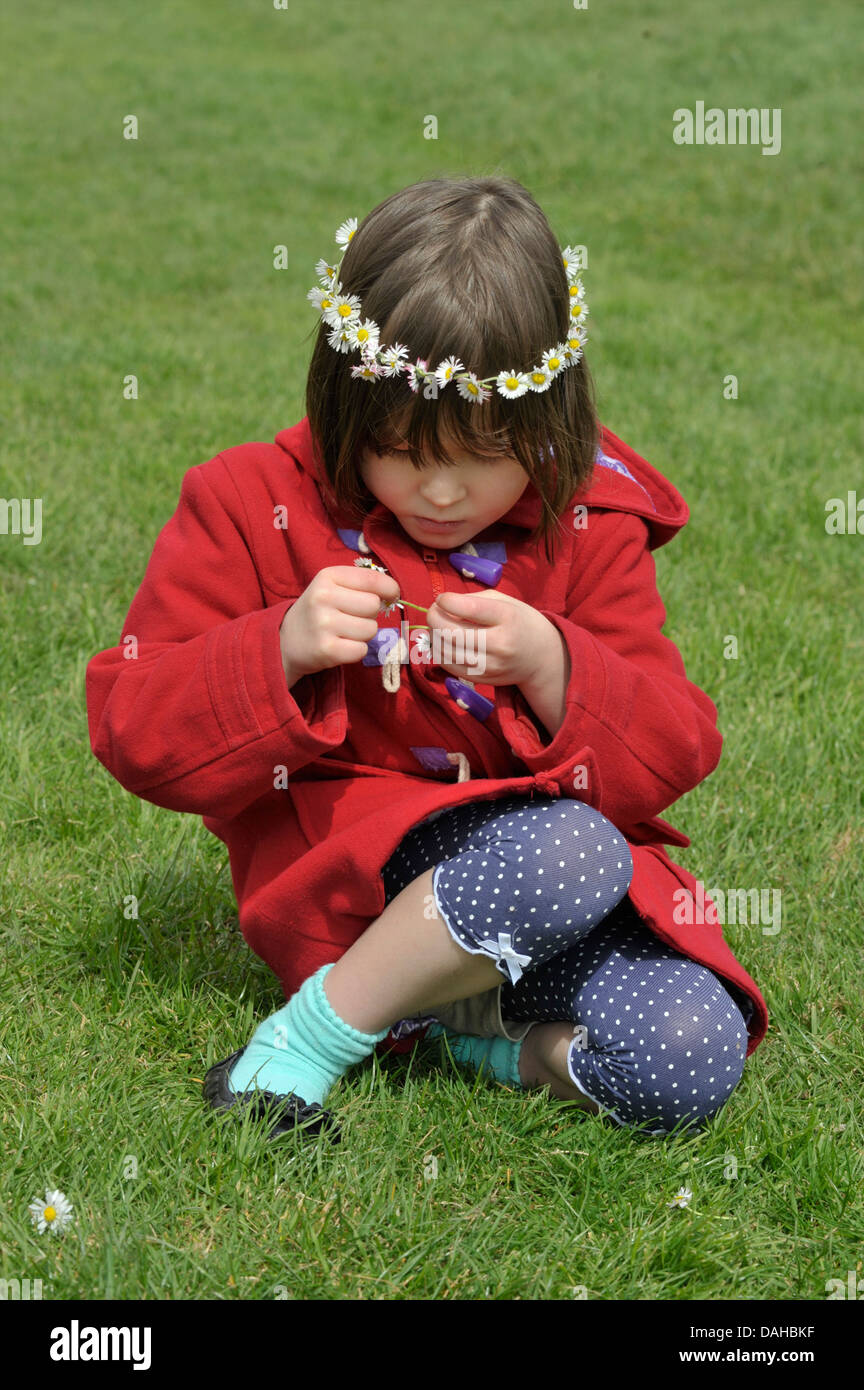 Sechs Jahre alten Mädchen, das eine Daisy-Chain auf dem Rasen. Model Released Stockfoto