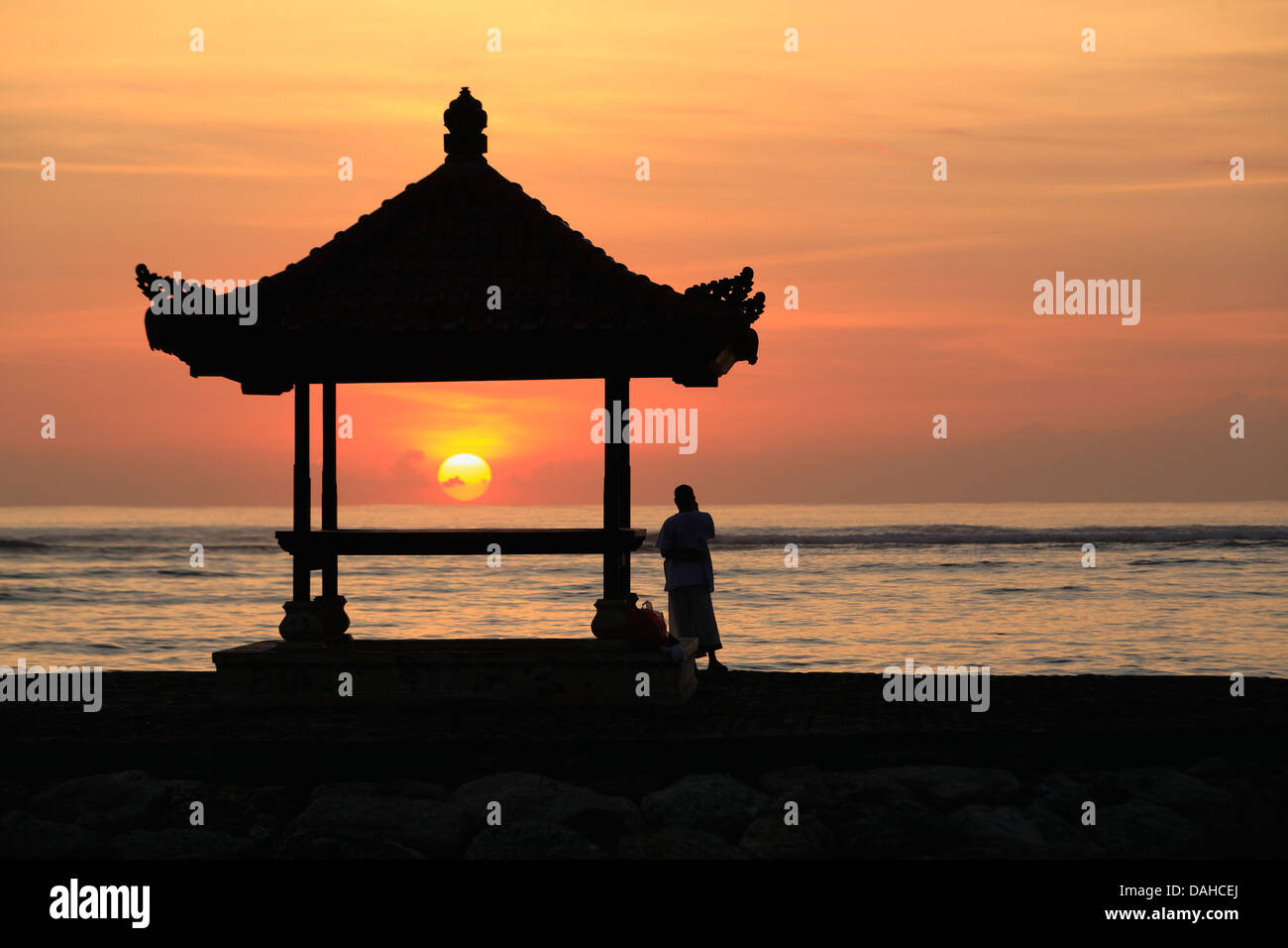 Eine Person neben einem Balinesischen Pagode stehen am Strand von Sanur, Bali. Bei Sonnenaufgang. Bali, Indonesien Stockfoto