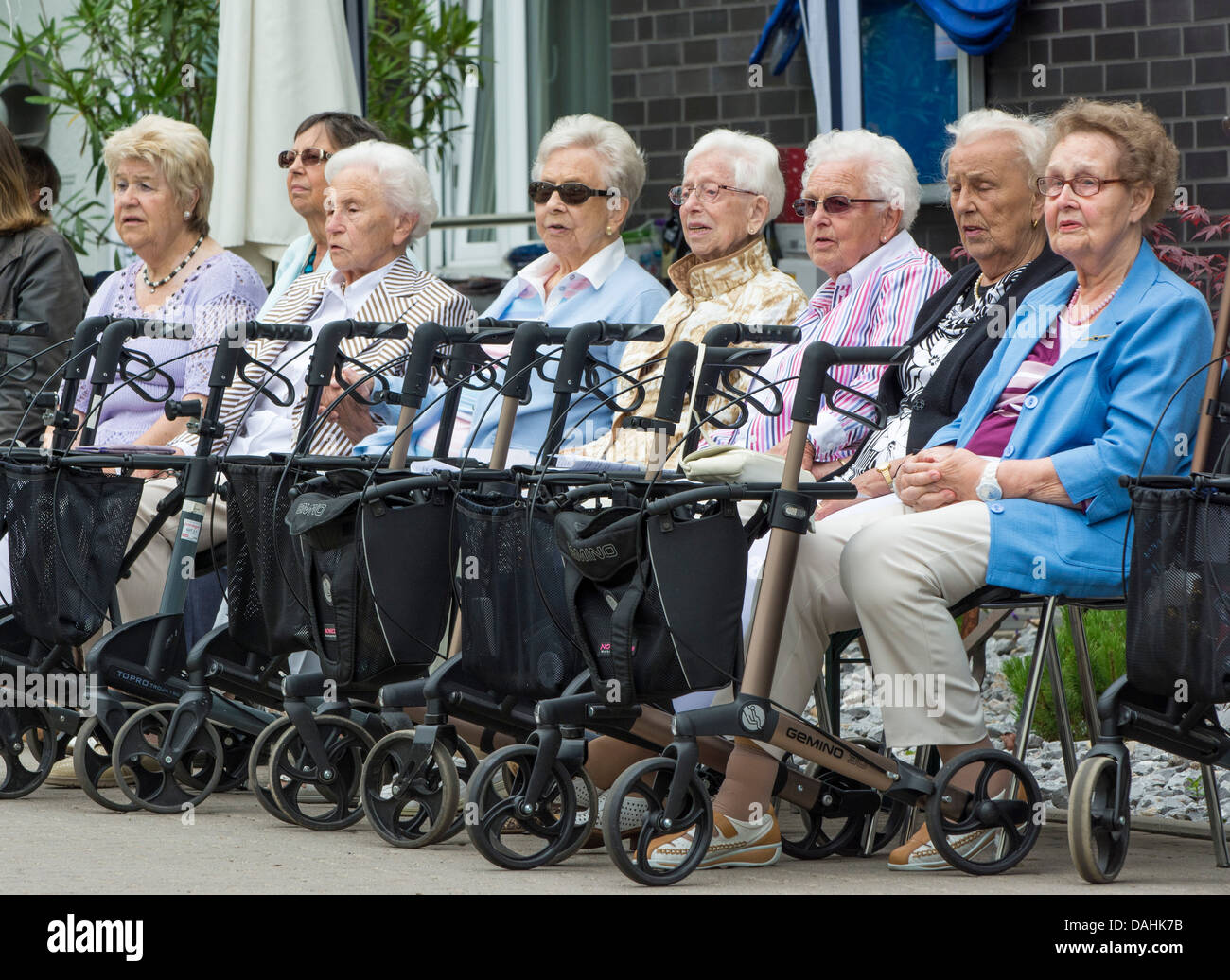 Acht alte Frauen sitzen vor einer Seniorenresidenz mit ihren Rollatoren / Wanderer auf Rädern / Gehhilfe vor ihnen. Stockfoto